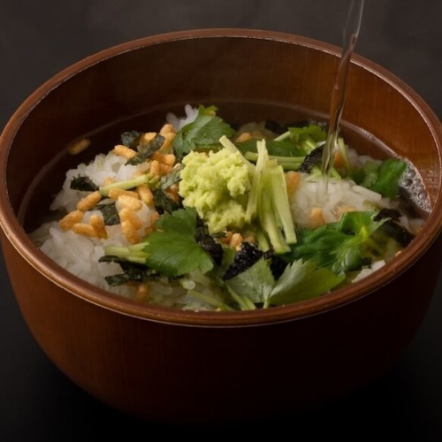 だしが注がれるお茶漬け。ワサビや三つ葉、あられがご飯に乗っている。